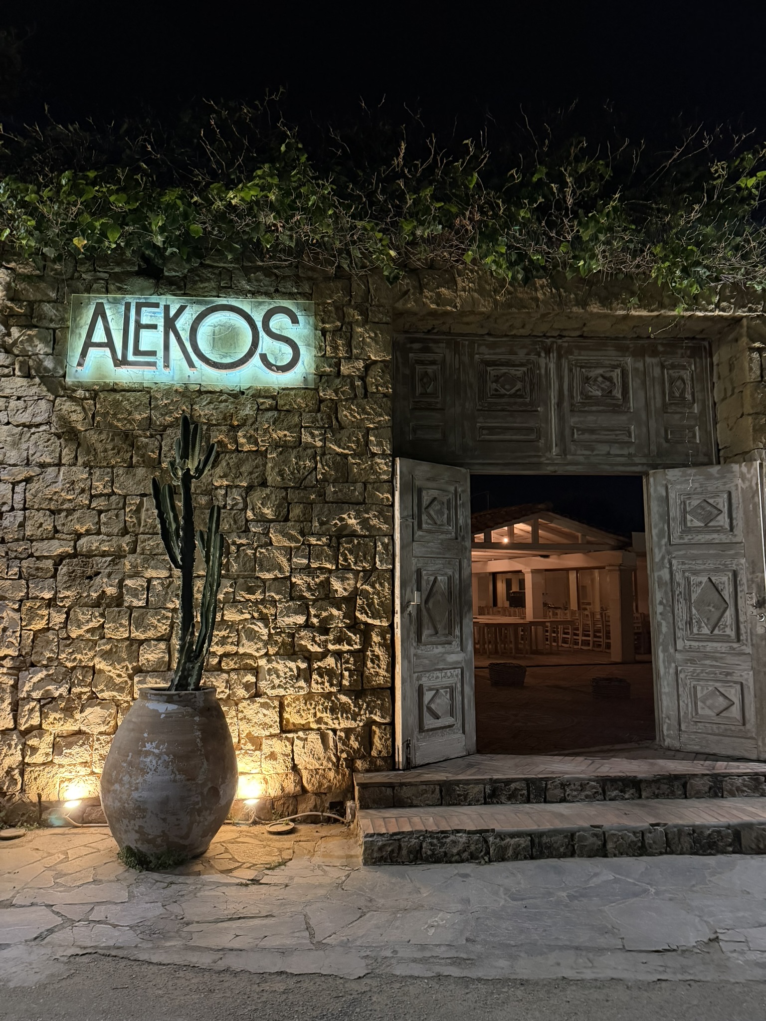 The entrance to Alekos — stone wall, neon sign, open doors